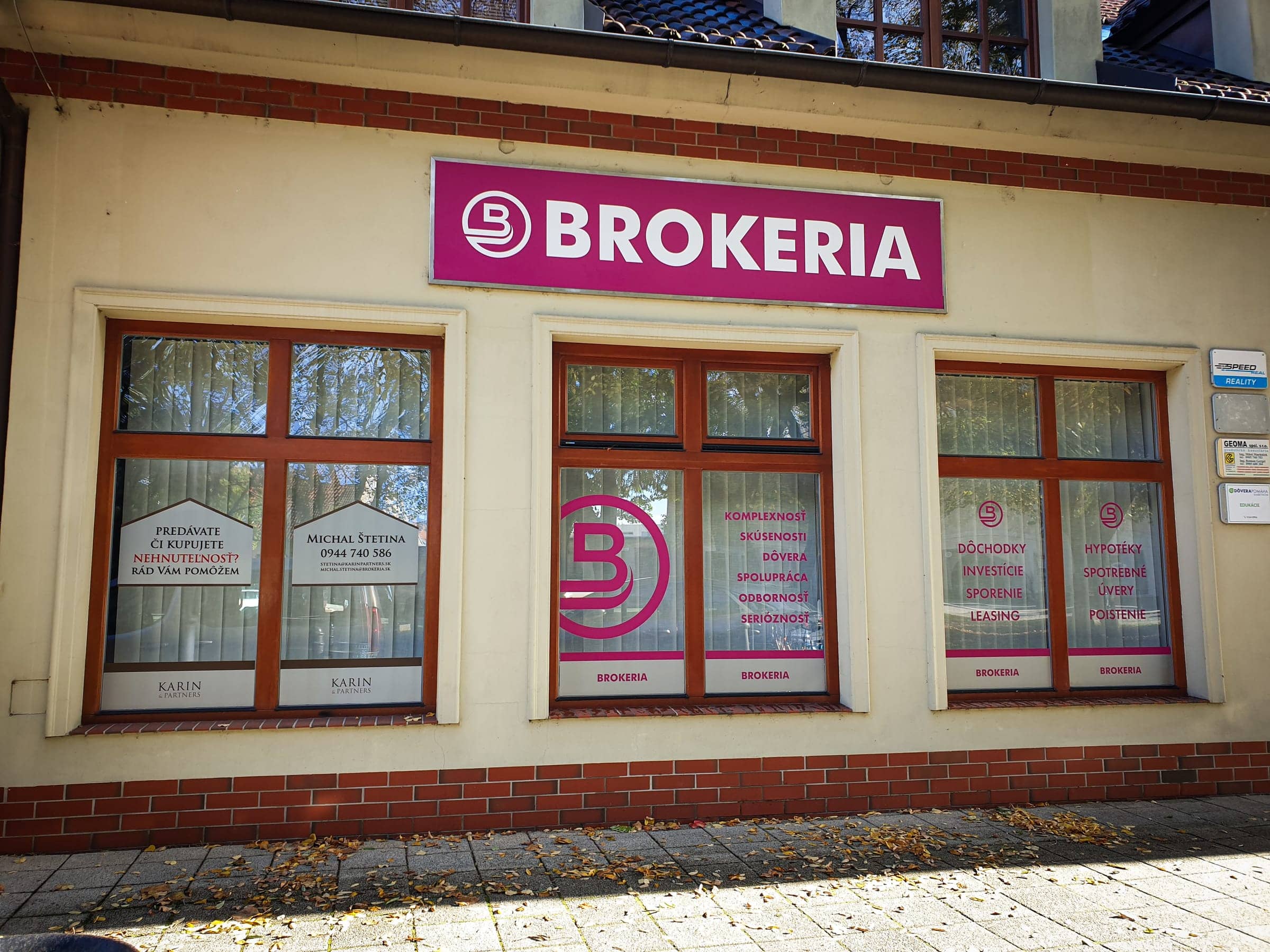 Pobočka BROKERIA s firemnou tabuľou nad oknami a polepom výkladov s logom a službami