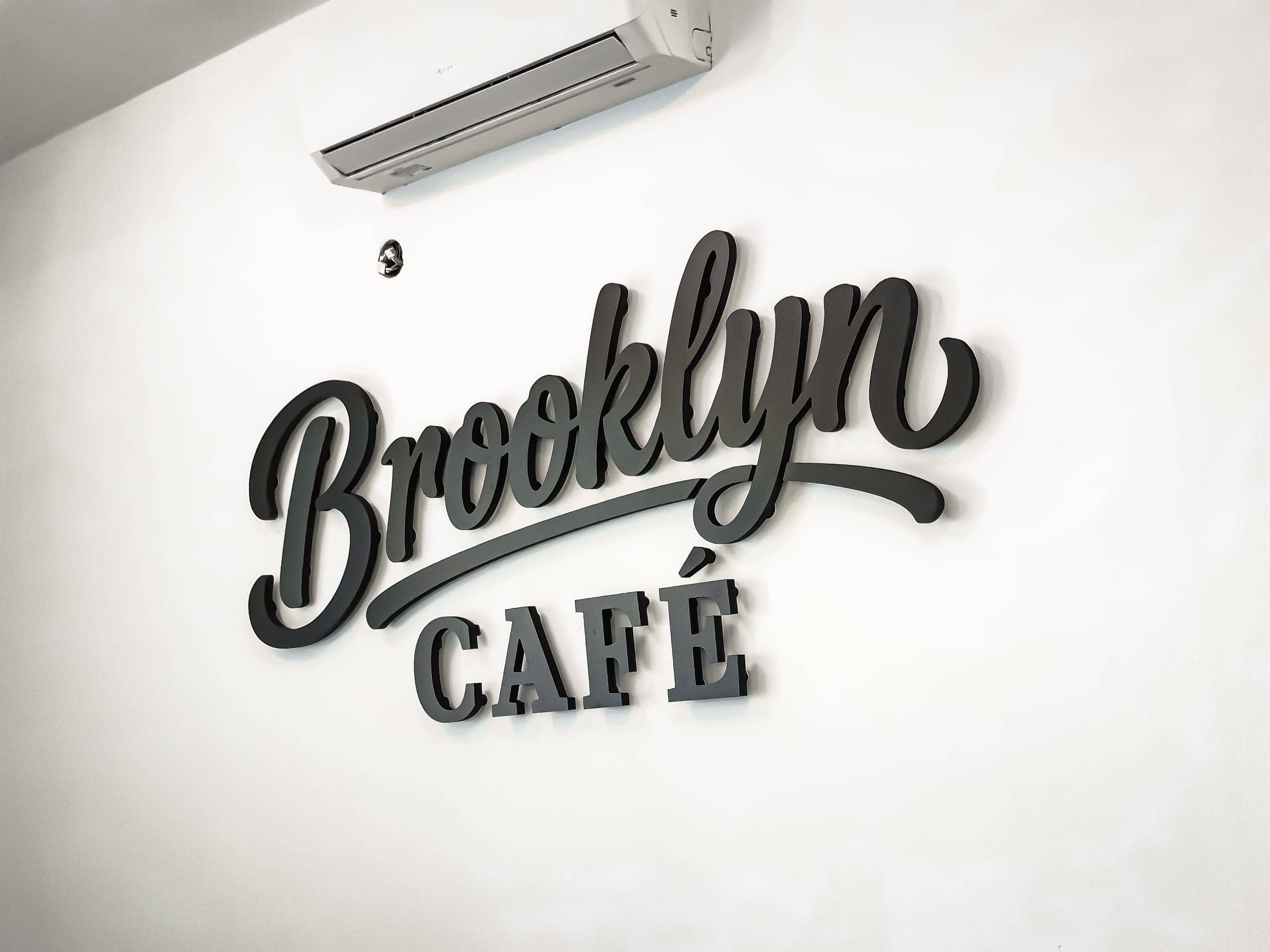 Priestorové 3D logo Brooklyn Café z tmavosivých písmen na bielej stene kaviarne