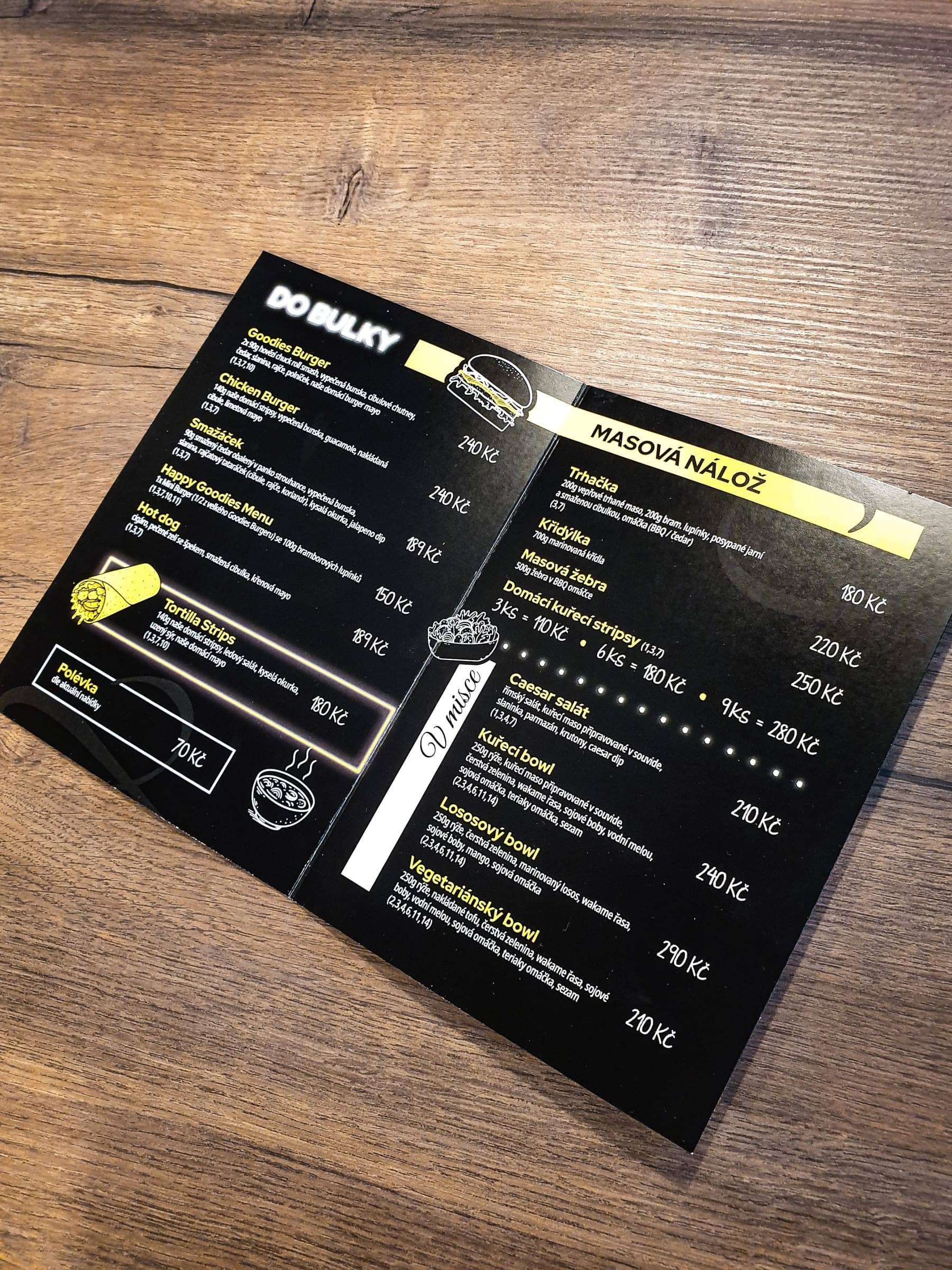 Tlačené jedálne menu Goodies Bistro v čiernom dizajne so žltými akcentmi na drevenom stole