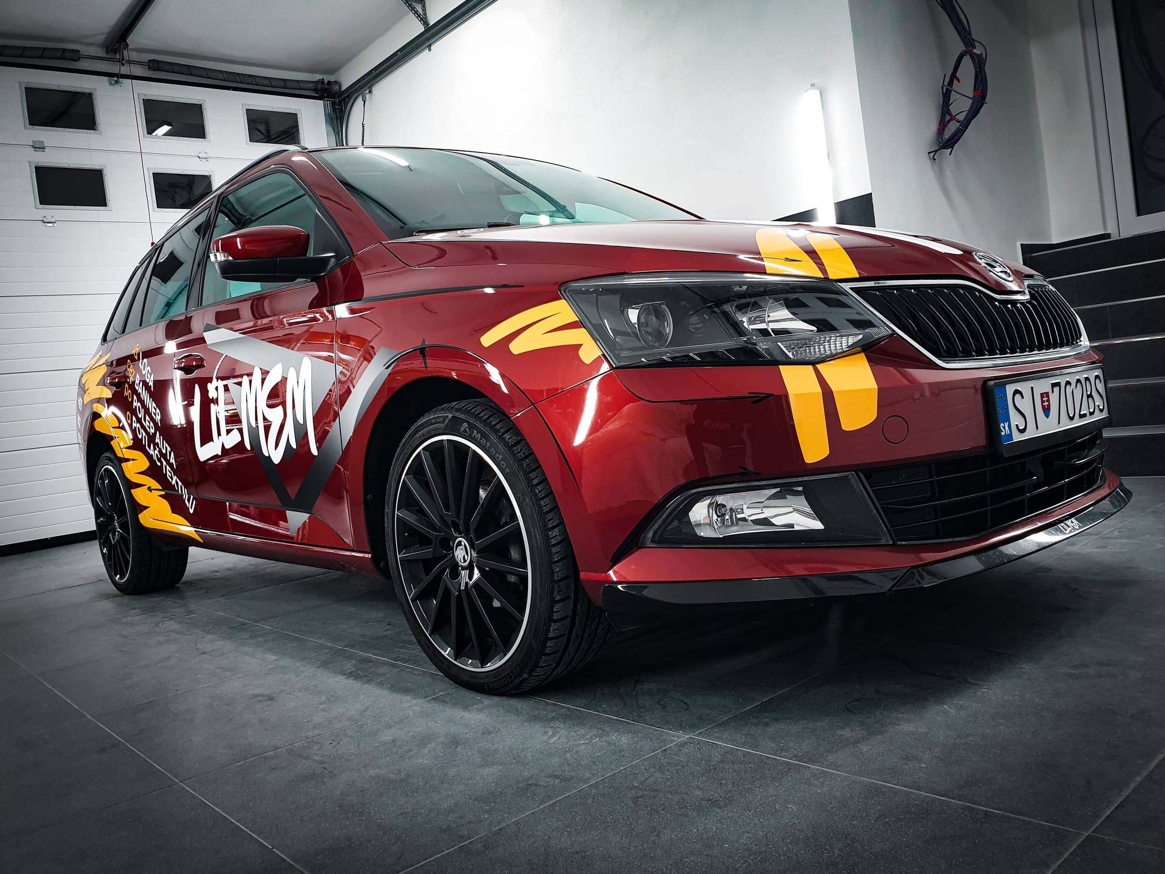 Červená Škoda Fabia Combi s firemným polepom LIL MEM v dielni, predná trojštvrtka