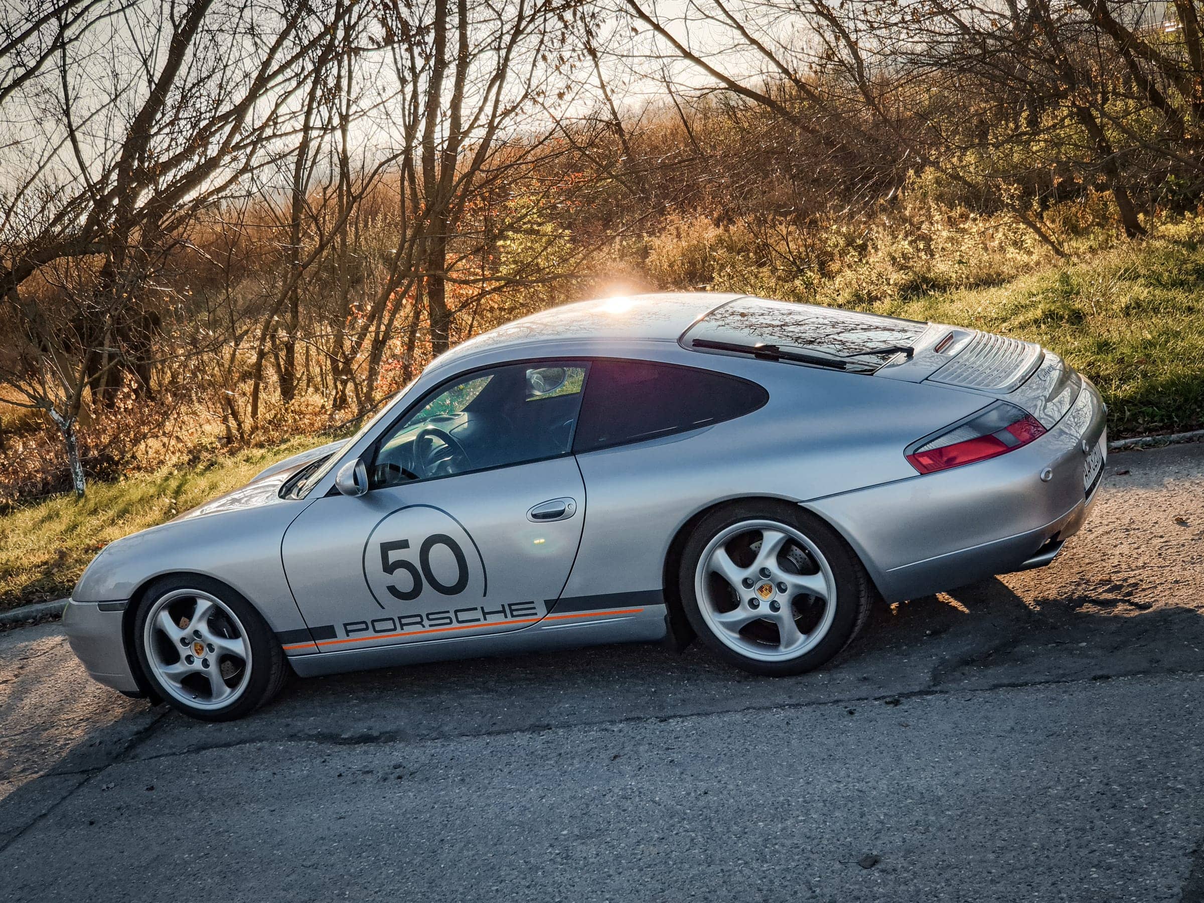 Strieborné Porsche 911 s retro polepom a štartovým číslom 50 pri západe slnka, pohľad zhora zboku