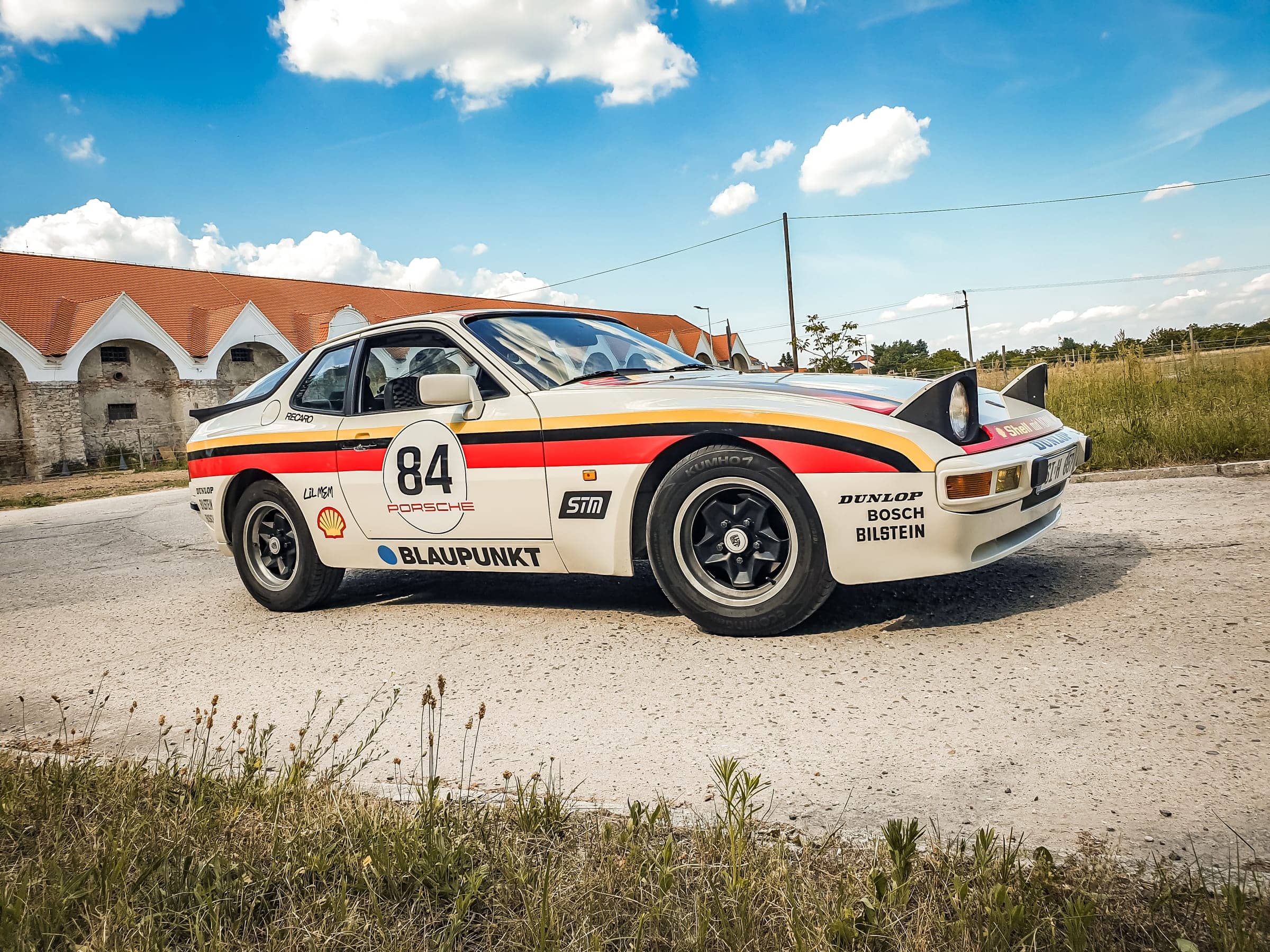 Biele Porsche 944 s retro pretekárskym polepom v nemeckých farbách, číslom 84 a logami sponzorov pri statku