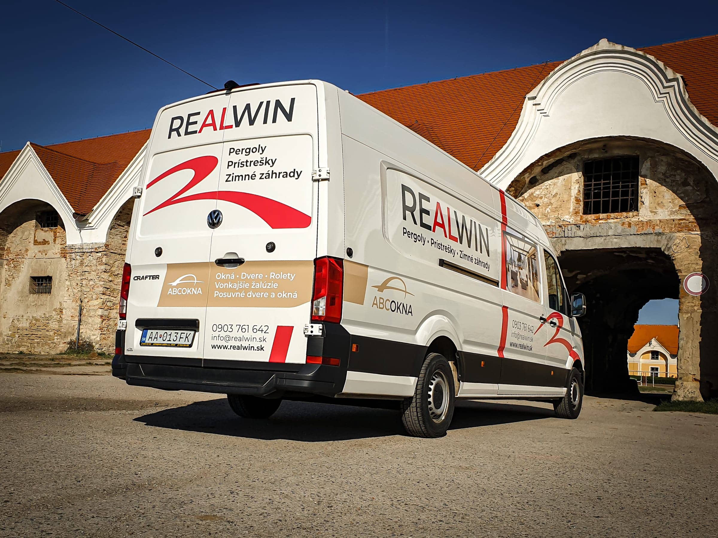 Dodávka VW Crafter s firemným polepom REALWIN – pergoly, prístrešky, zimné záhrady – zozadu pred kamennou bránou statku